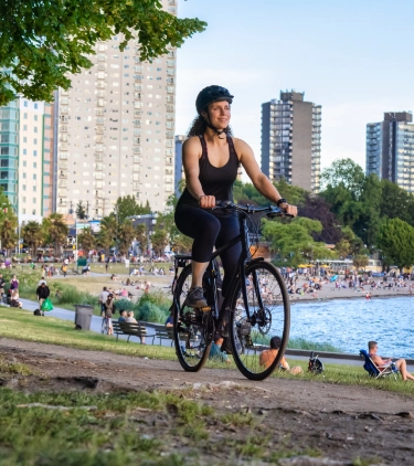Young woman with travel insurance for Canada biking in a park with Vancouver in the background