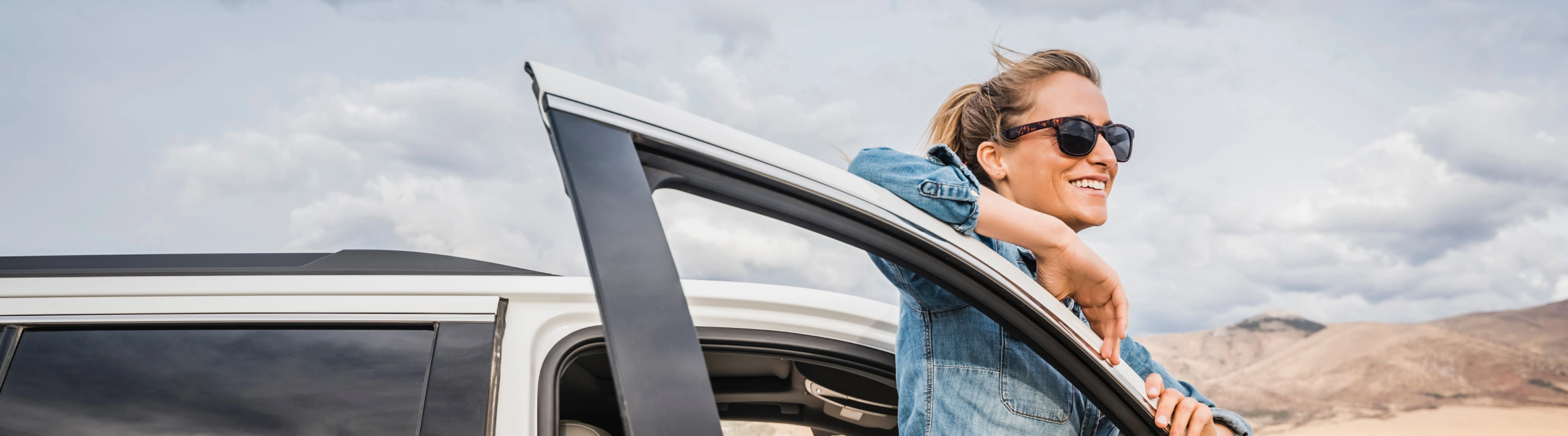 Woman, with travel insurance for Nevada, standing behind an open car door and looking at the desert scenery