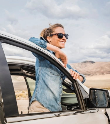 Woman, with travel insurance for Nevada, standing behind an open car door and looking at the desert scenery