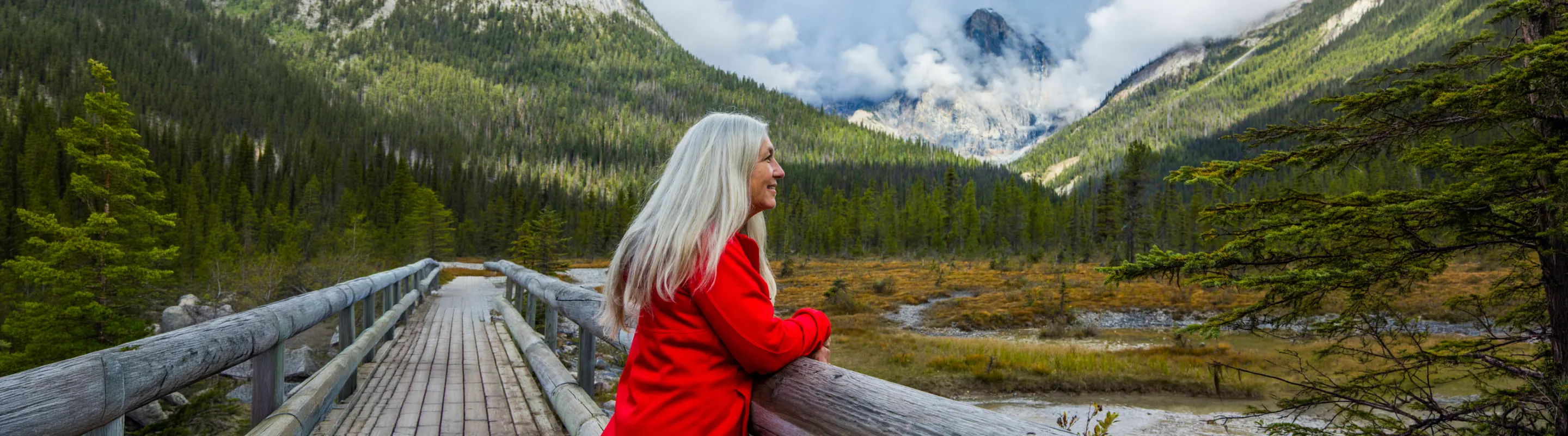 Senior woman on a bridge overlooking the mountains with travel insurance for Canada