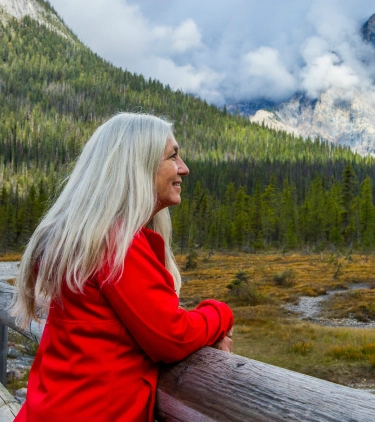 Senior woman on a bridge overlooking the mountains with travel insurance for Canada