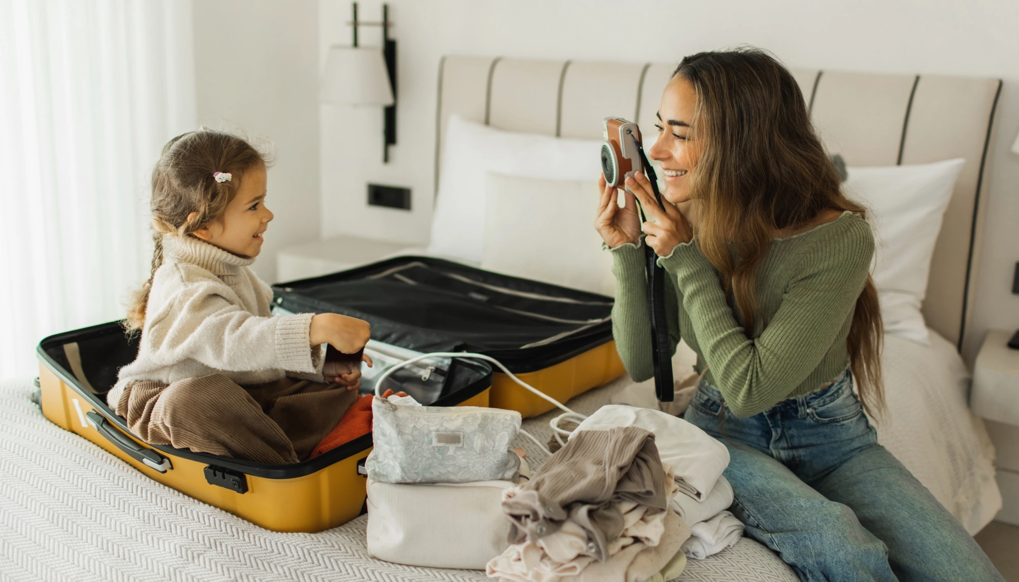 woman holding a camera and taking a picture of her daughter in a suitcase, helping her overcome her travel anxiety