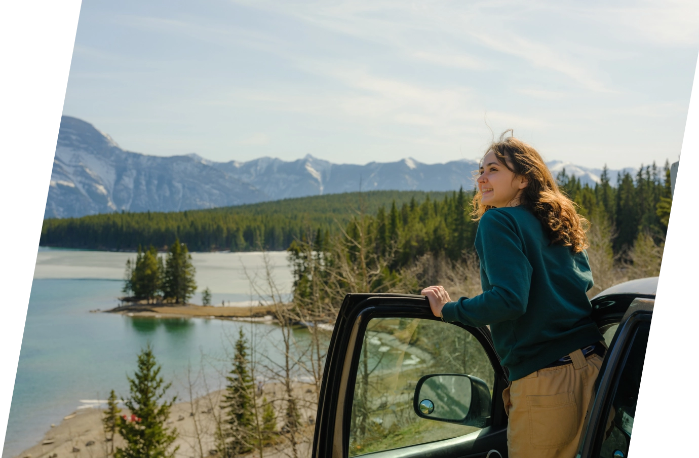 a young woman with road trip travel insurance steps out of the front door of her car to soak up alpine scenery