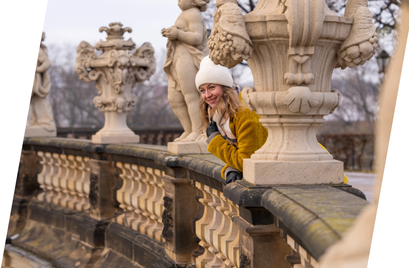 Young woman with travel insurance for Germany leaning against a stone railing between statues and smiling in Dresden