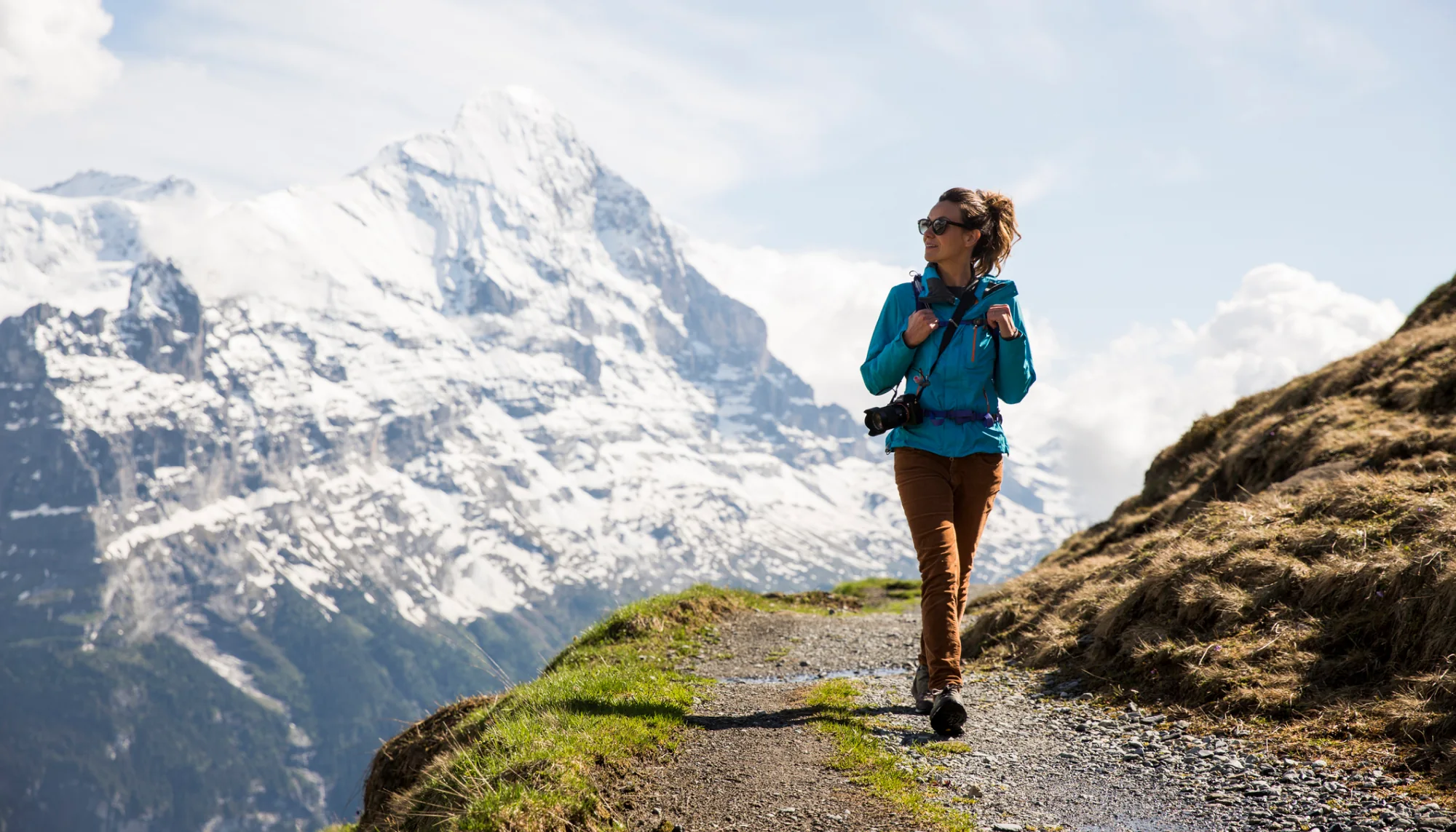 a young woman wearing a blue jacket hikes a mountain trail after looking up the best places to travel as a solo female
