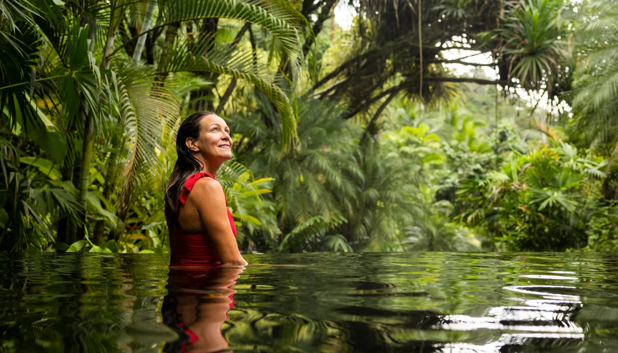 Woman looking up at trees from a pool in the jungle while being a responsible traveler on vacation