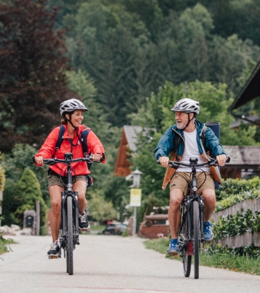 a man and women with travel insurance for Austria, biking through a small Austrian town in the country