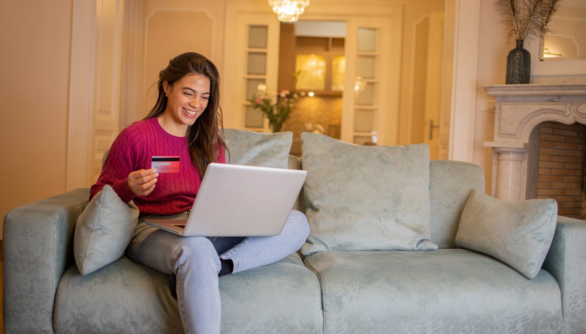 young woman at home holding a credit card while using her laptop to buy travel insurance plans