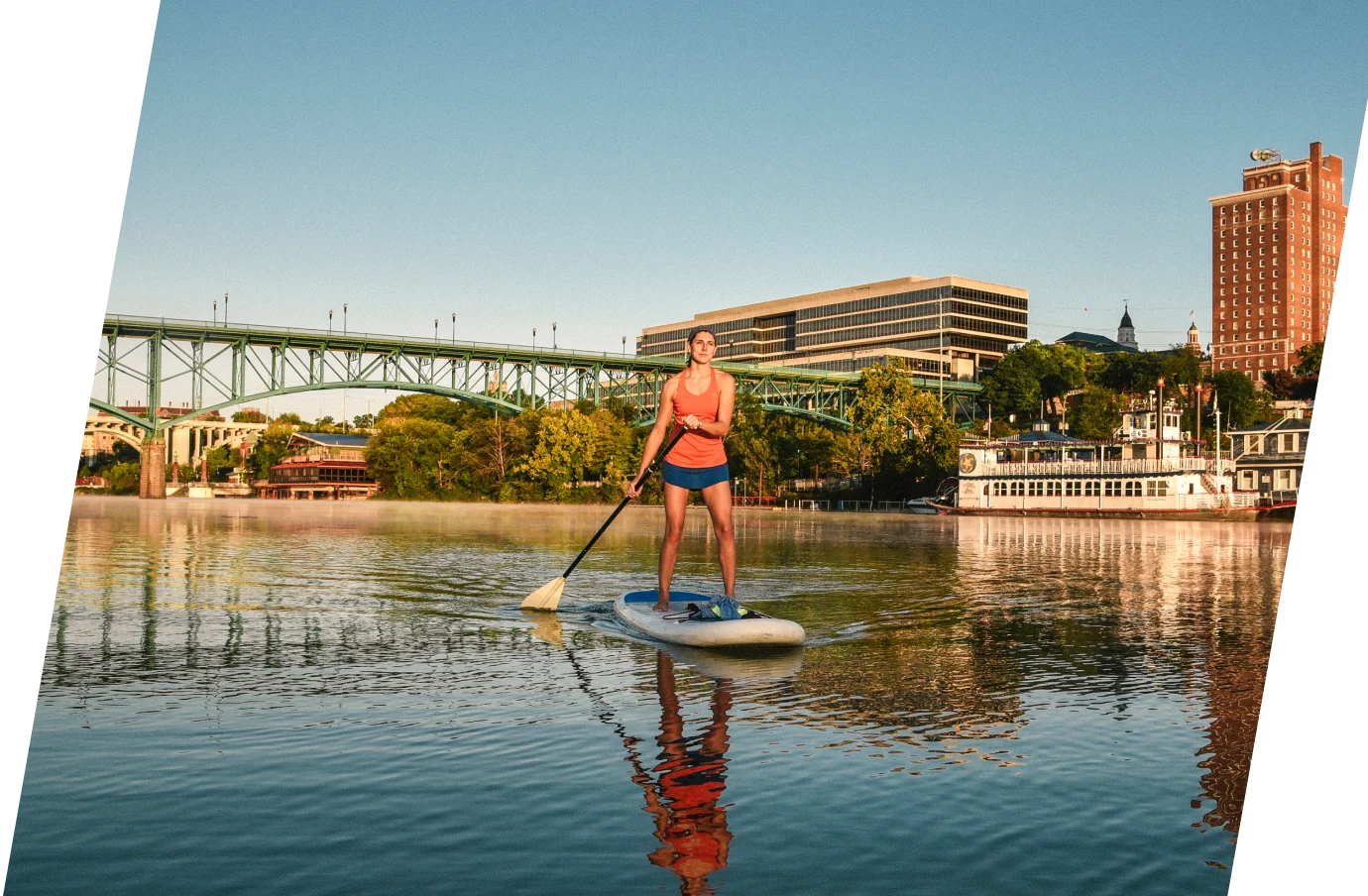 Woman with travel insurance for Tennessee paddleboarding on the river in front of the city and bridge