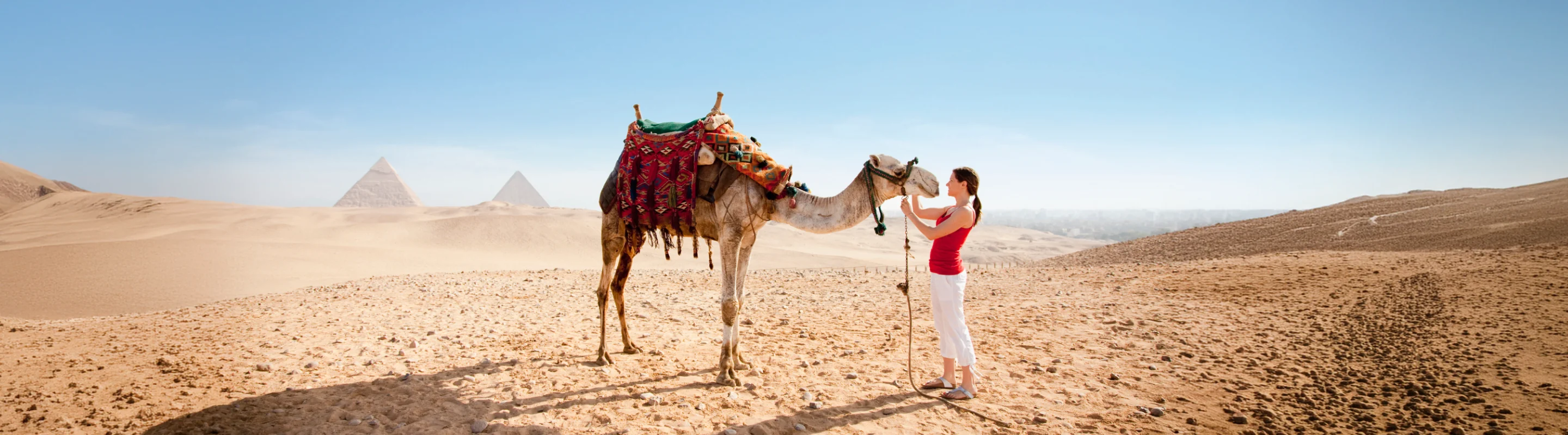 Woman petting a camel in the desert with travel insurance for Africa