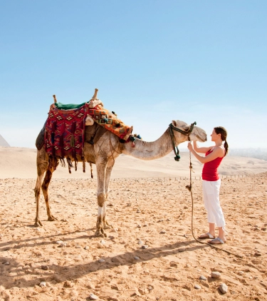Woman petting a camel in the desert with travel insurance for Africa