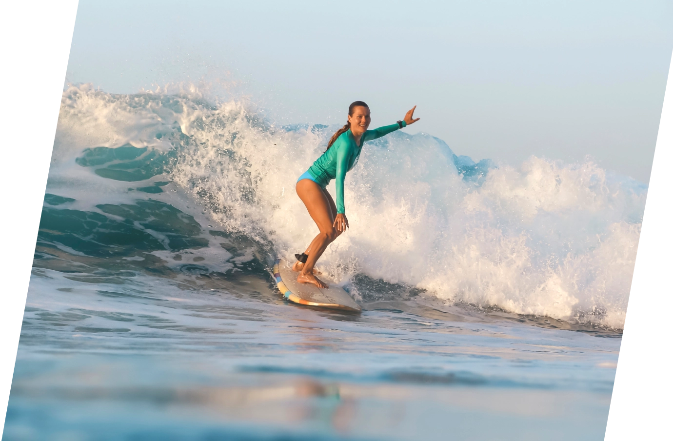 Woman with travel insurance for Bali surfing with a teal long sleeve rash guard