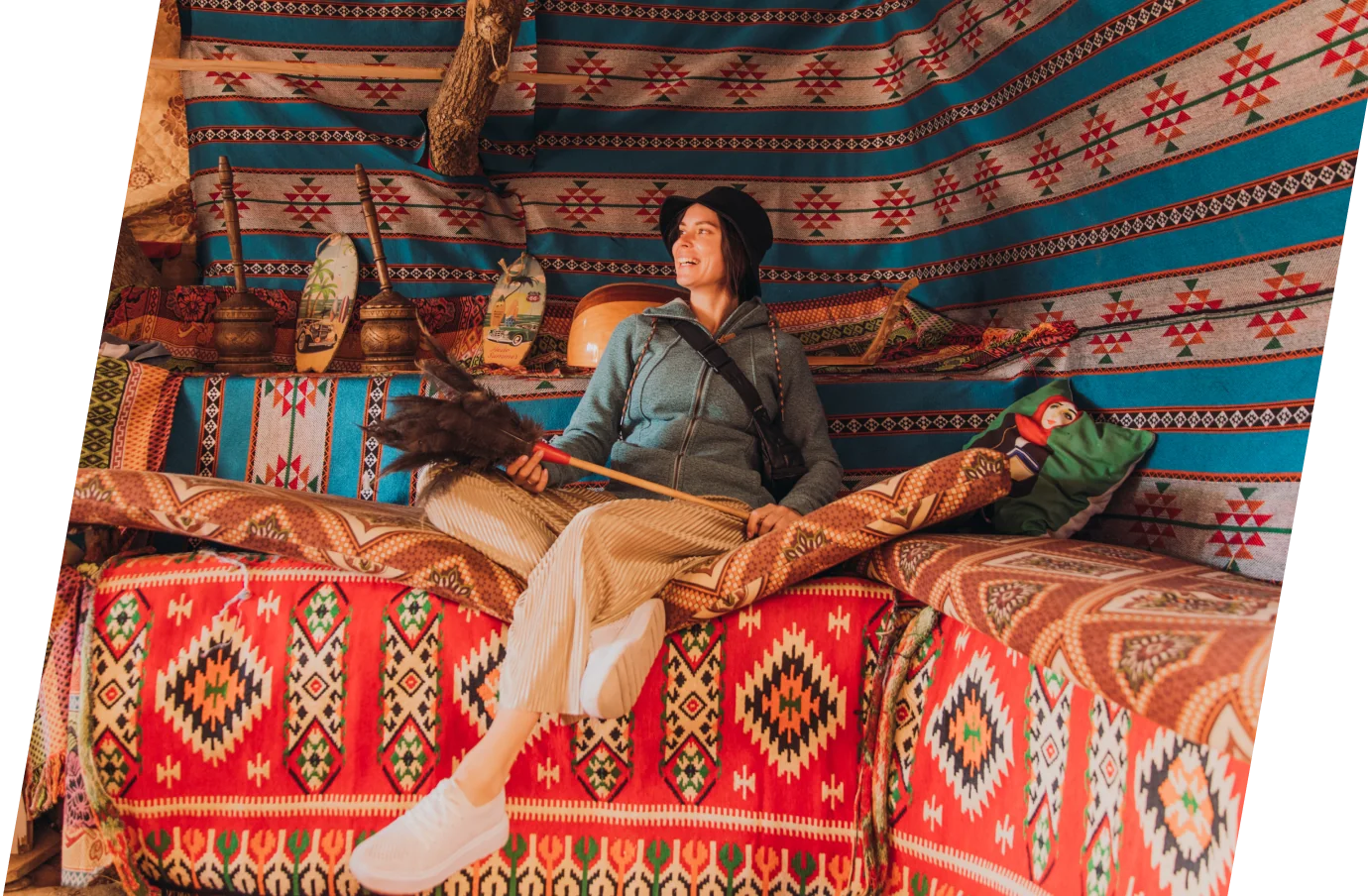 a woman with travel insurance for Jordan sits in a traditional Bedouin-style tent holding a feather duster