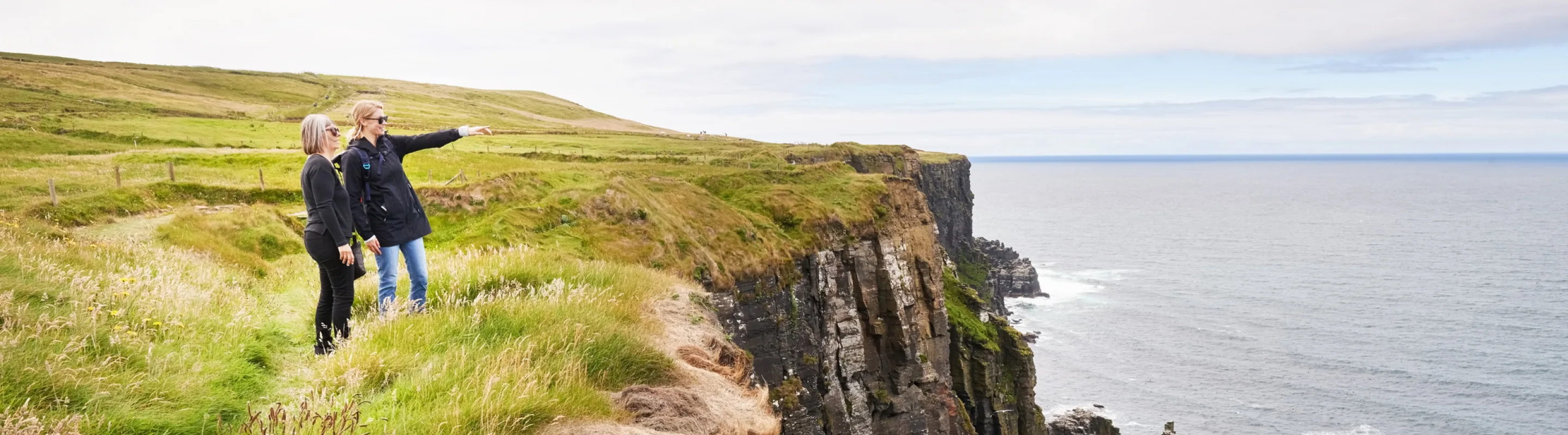 Two women with travel insurance for Ireland, enjoying views at the Cliffs of Moher 