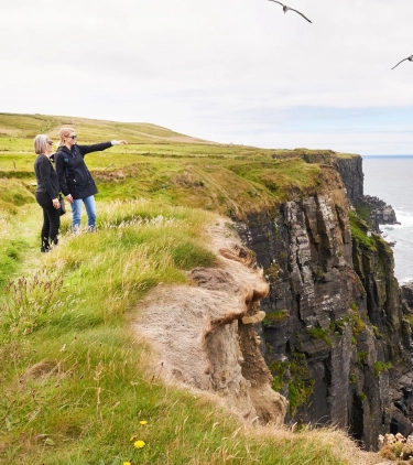 Two women with travel insurance for Ireland, enjoying views at the Cliffs of Moher 