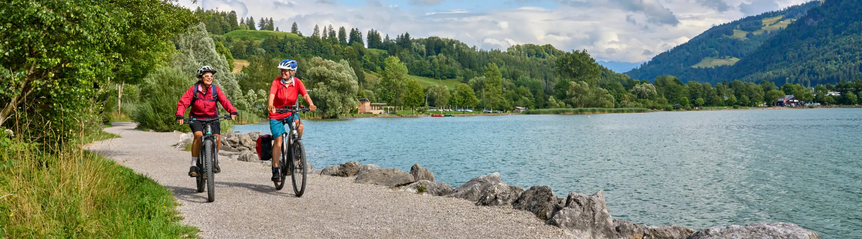Two middle-aged women with travel insurance for Germany biking along Lake Alpsee in Bavaria