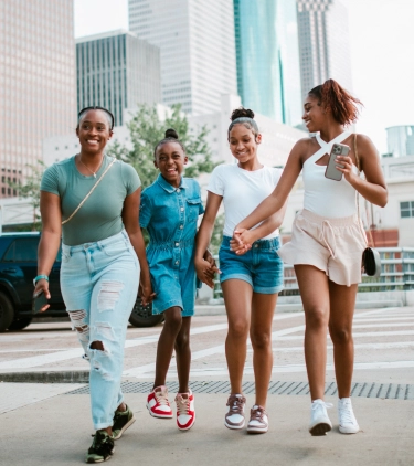 two older sisters hold their younger sisters' hand as they cross a street in Houston, insured with travel insurance for Texas