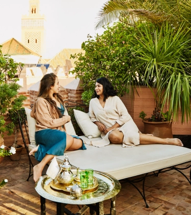 Two brunette women with travel insurance for Morocco lounge in a warm, intimate garden courtyard