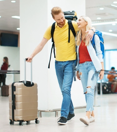 a young couple with cruise travel insurance and large backpacks walk alongside one another through an airport terminal 