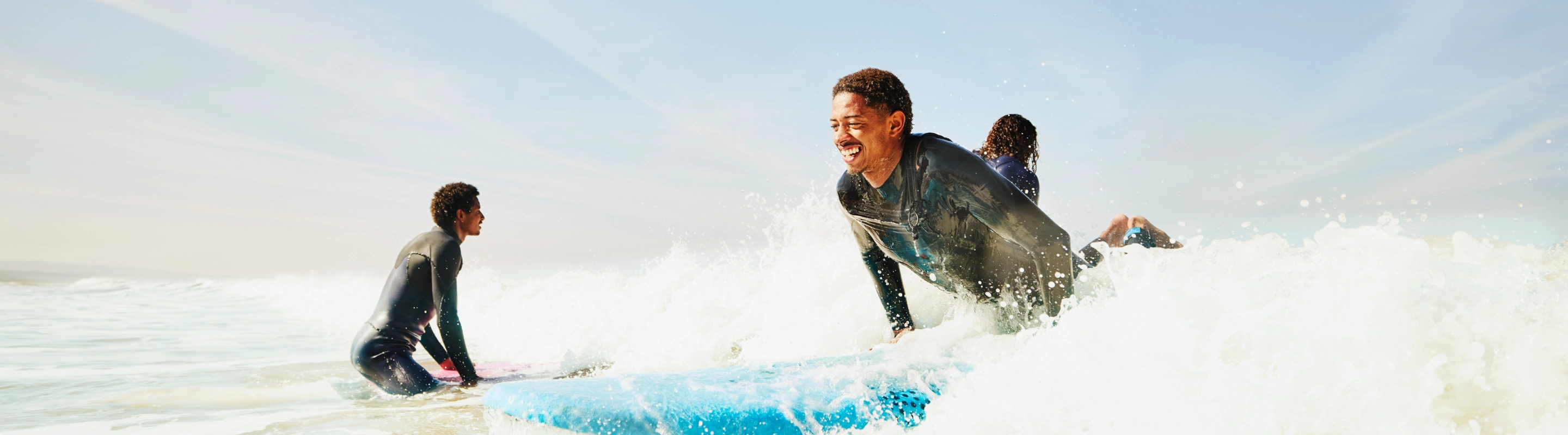 a young, mixed-race man with travel insurance for Morocco wears a wetsuit and catches a wave on his surfboard