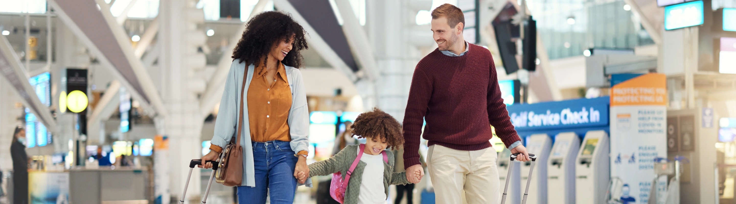 a family with travel insurance for cultural trips walks through an airport terminal's self-check-in area with their suitcases