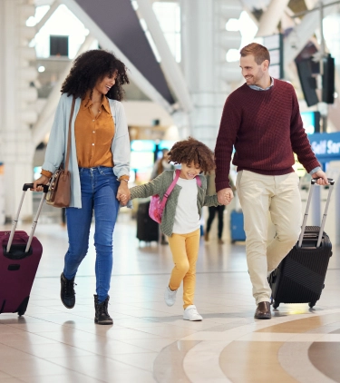 a family with travel insurance for cultural trips walks through an airport terminal's self-check-in area with their suitcases