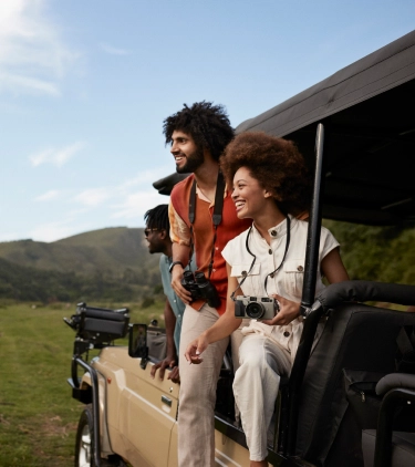 three mixed-race young adults with travel insurance for nature trips sightsee on a jeep safari in Africa 