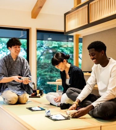 three young adults with travel insurance for wellness retreats smile as they partake in a traditional Japanese tea ceremony