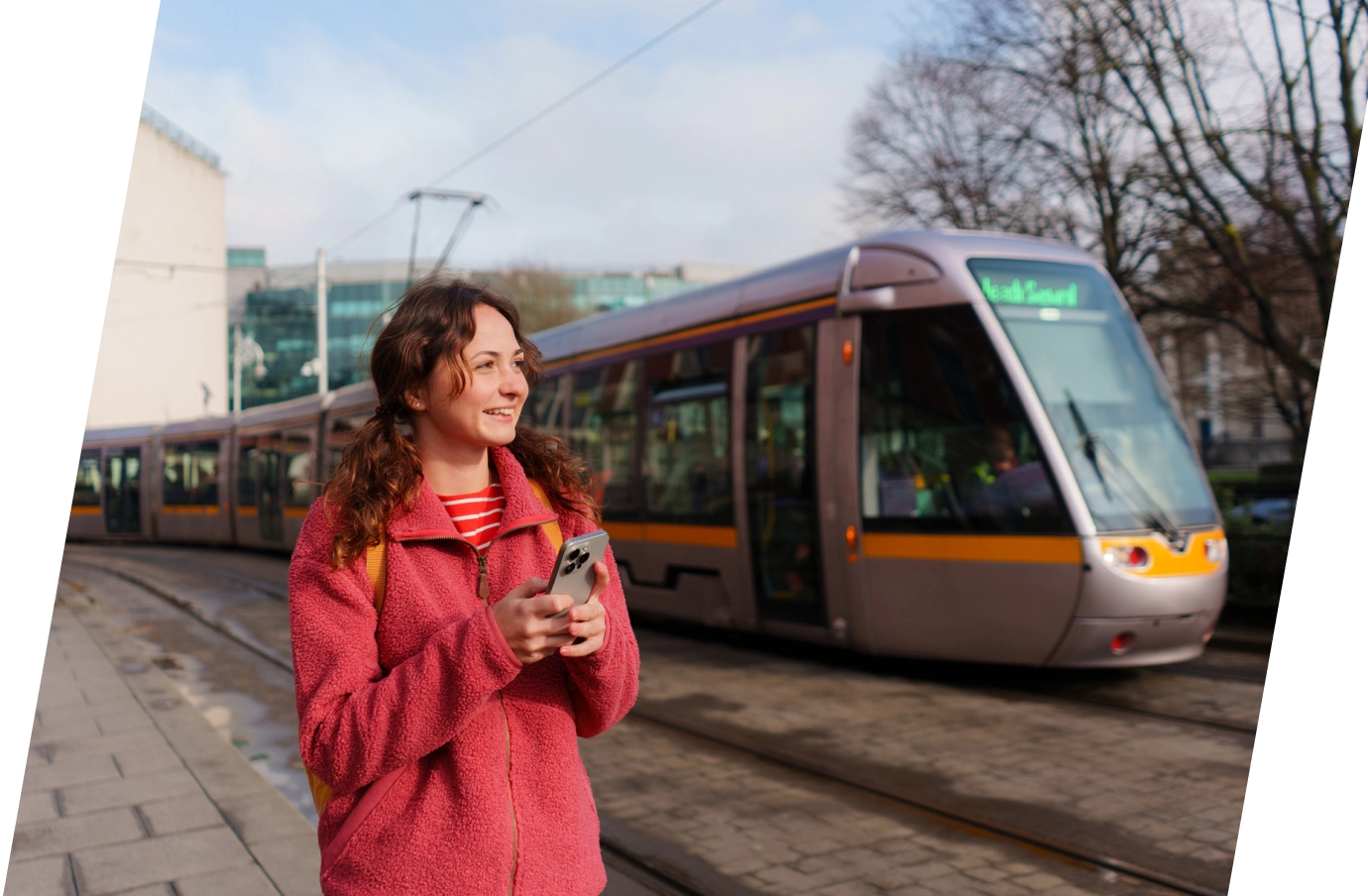 Woman with travel insurance for Ireland holding her phone and smiling while waiting for the tram to arrive