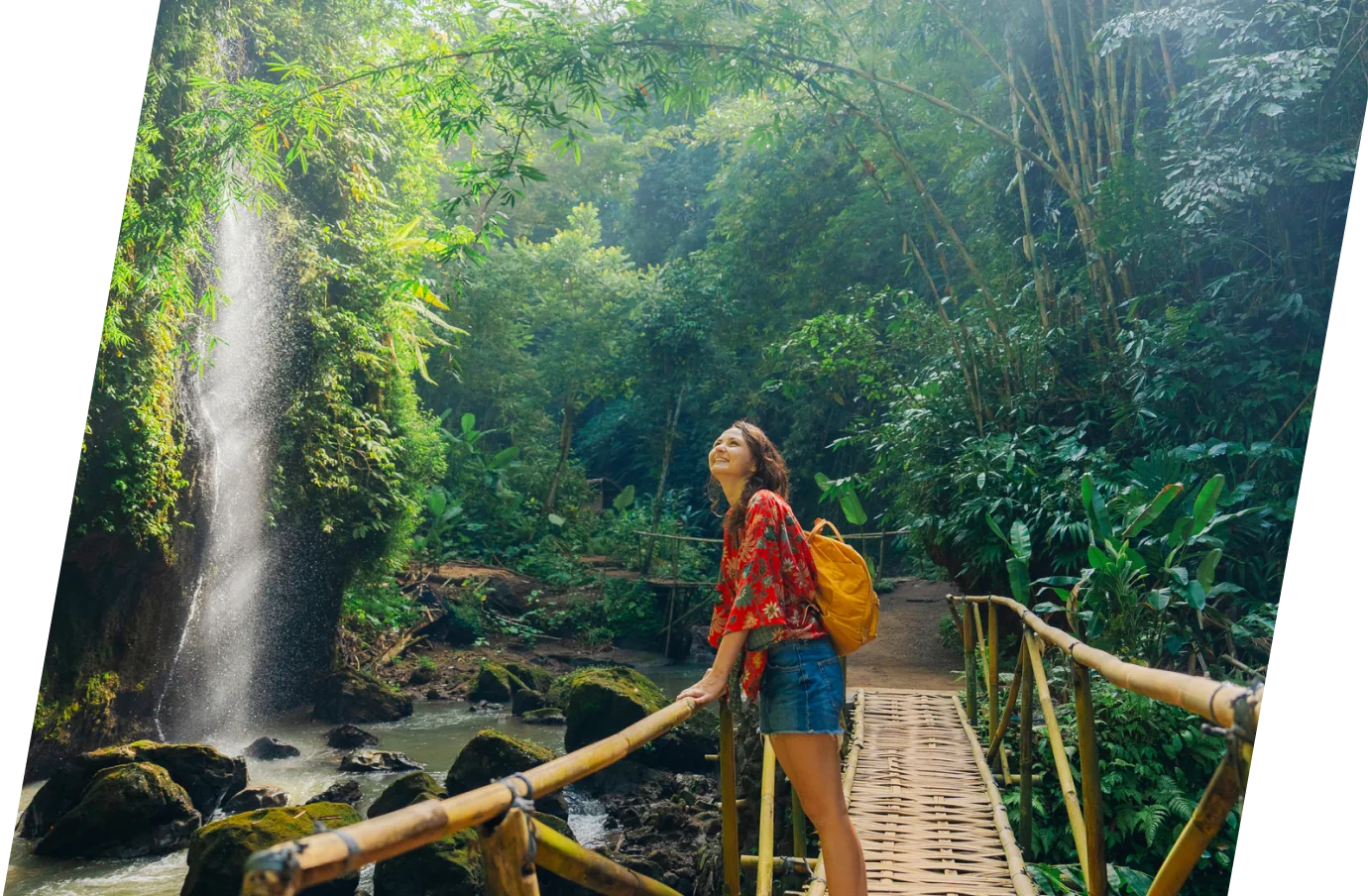 a young woman with travel insurance for nature trips stands on a bamboo bridge in a forest near a waterfall 
