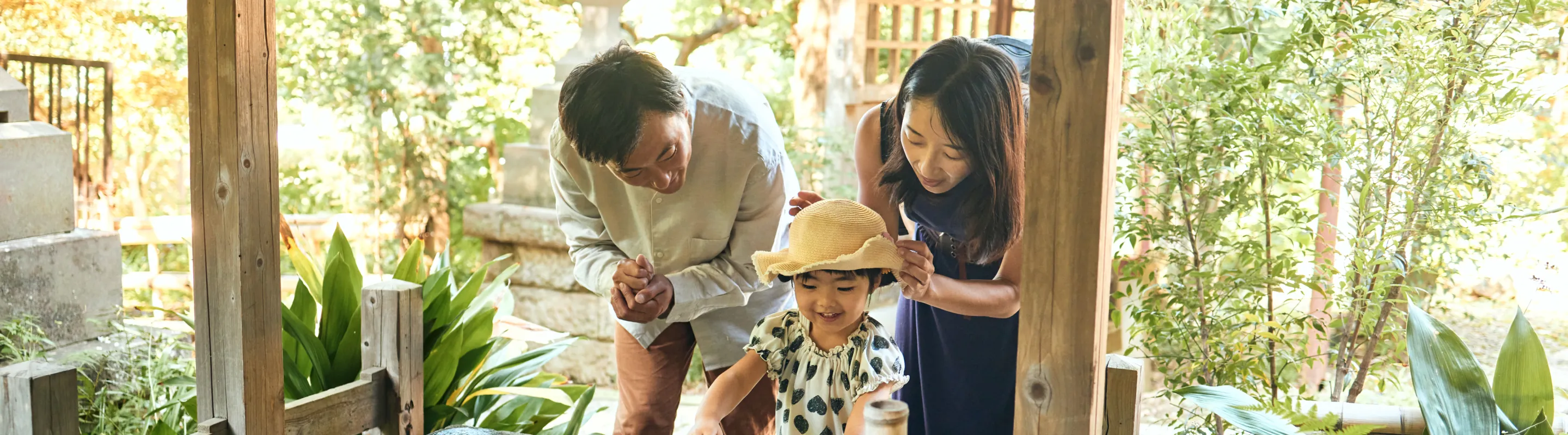 Asian parents with pilgrimage travel insurance walk through a sacred garden path with their daughter, surrounded by greenery 