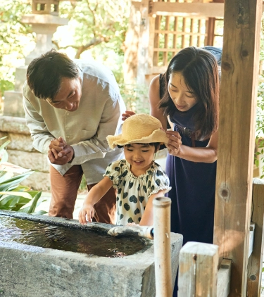 Asian parents with pilgrimage travel insurance walk through a sacred garden path with their daughter, surrounded by greenery 