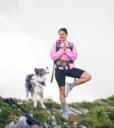 a woman hiker with travel insurance for wellness retreats practices yoga with her dog by her side on a mountain