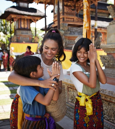 a mother with pilgrimage travel insurance offers a traditional greeting to ornate temple carvings with her son and daughter  