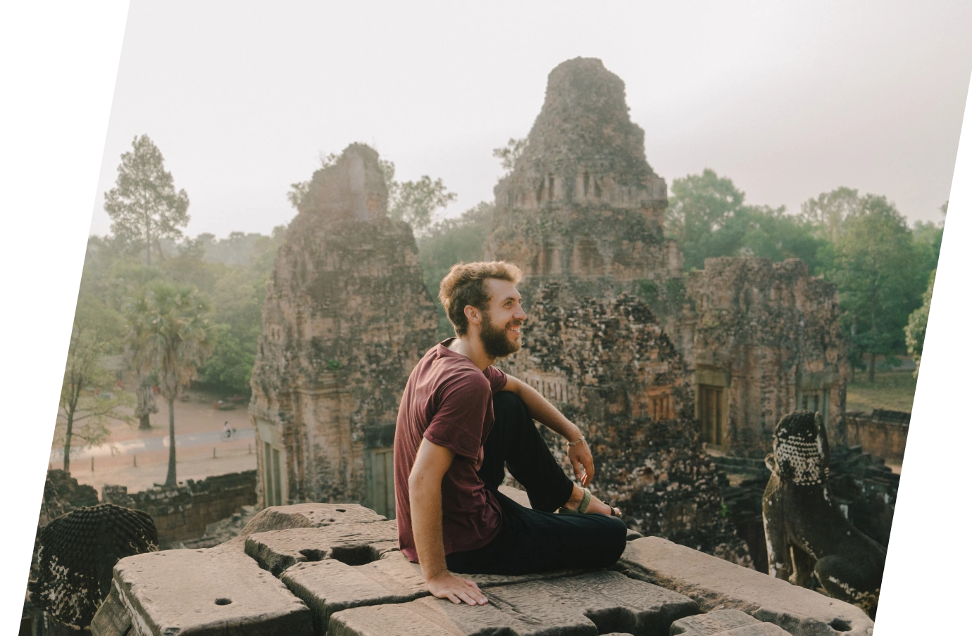a young adult man with pilgrimage travel insurance sits on a ledge overlooking the Angkor Wat Temple ruins in Cambodia 