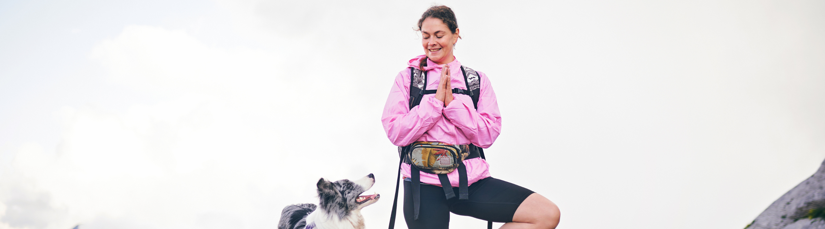 a hiker with travel insurance for wellness retreats practices yoga on the top of a mountain with her dog by her side