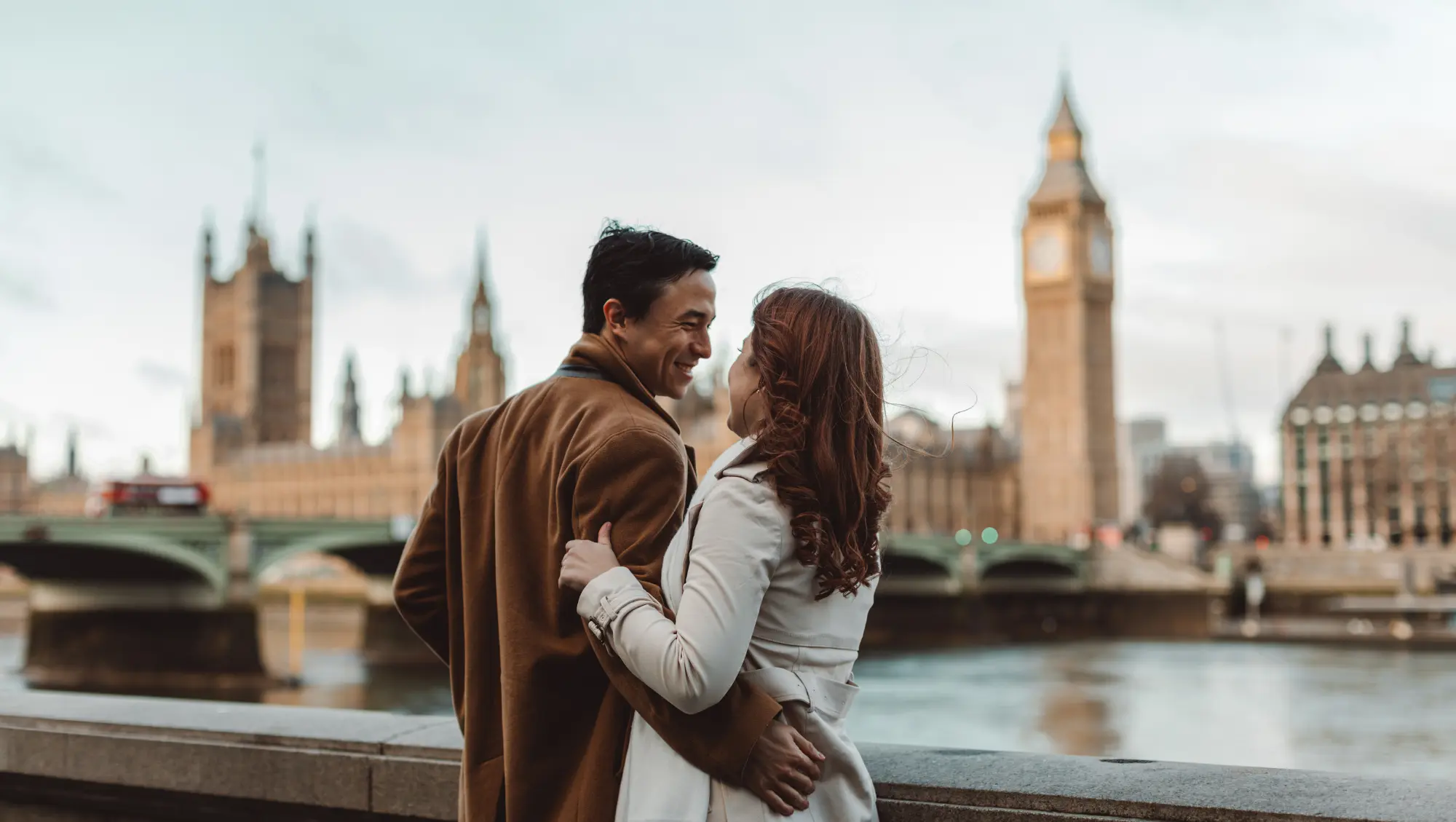 a young couple embraces by Big Ben and the river in London, one of the most romantic vacation destinations 