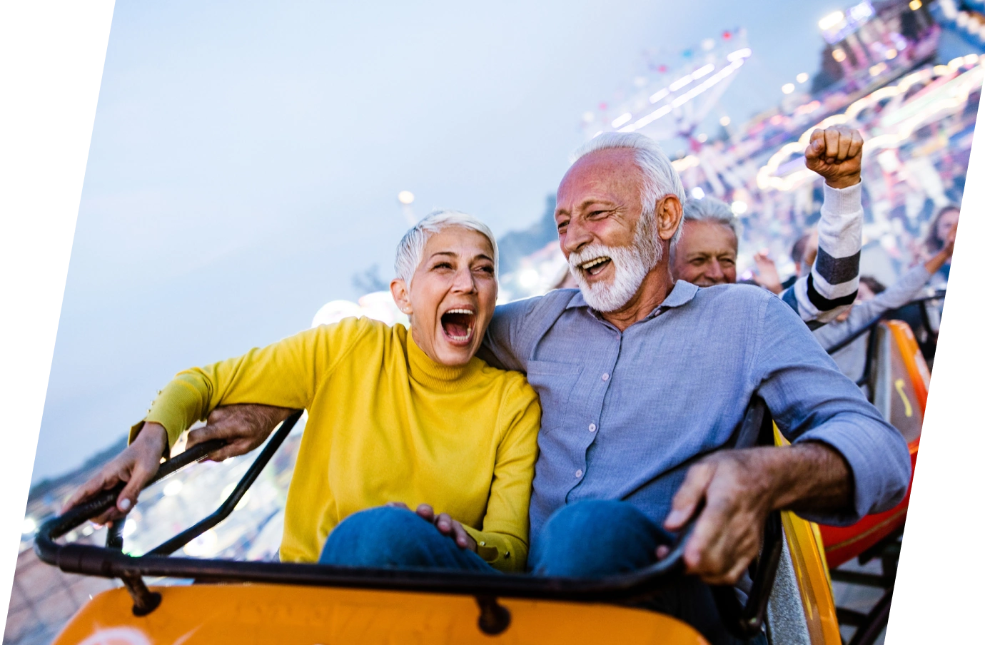 a senior couple with couples' travel insurance laughs as they ride on a roller coaster in an amusement park