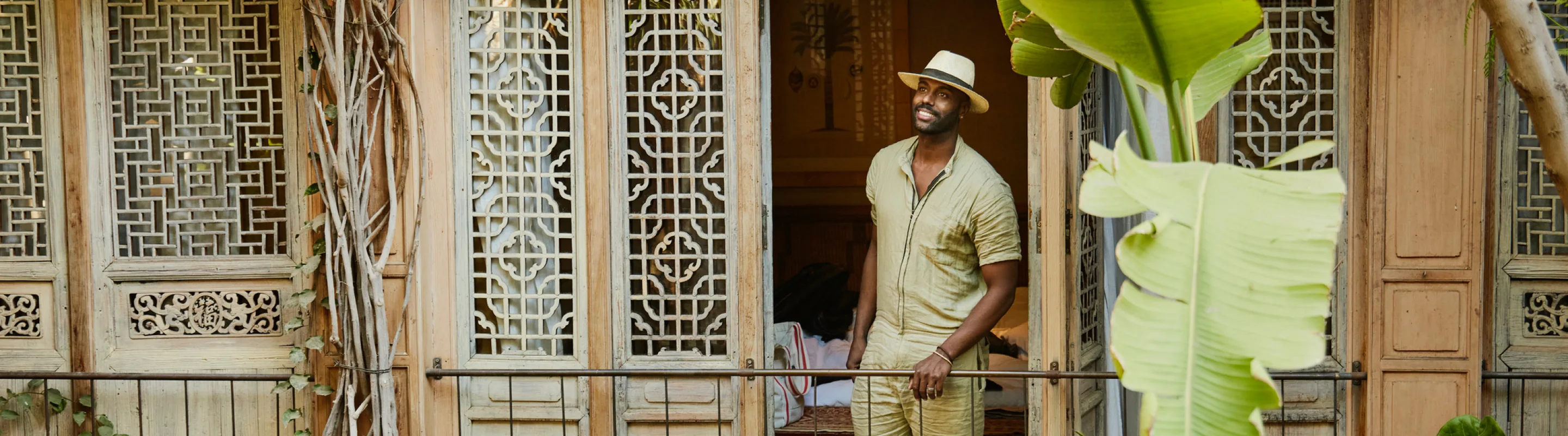 a young black man wearing a hat stands on a balcony outside his hotel room, insured with solo travel insurance 