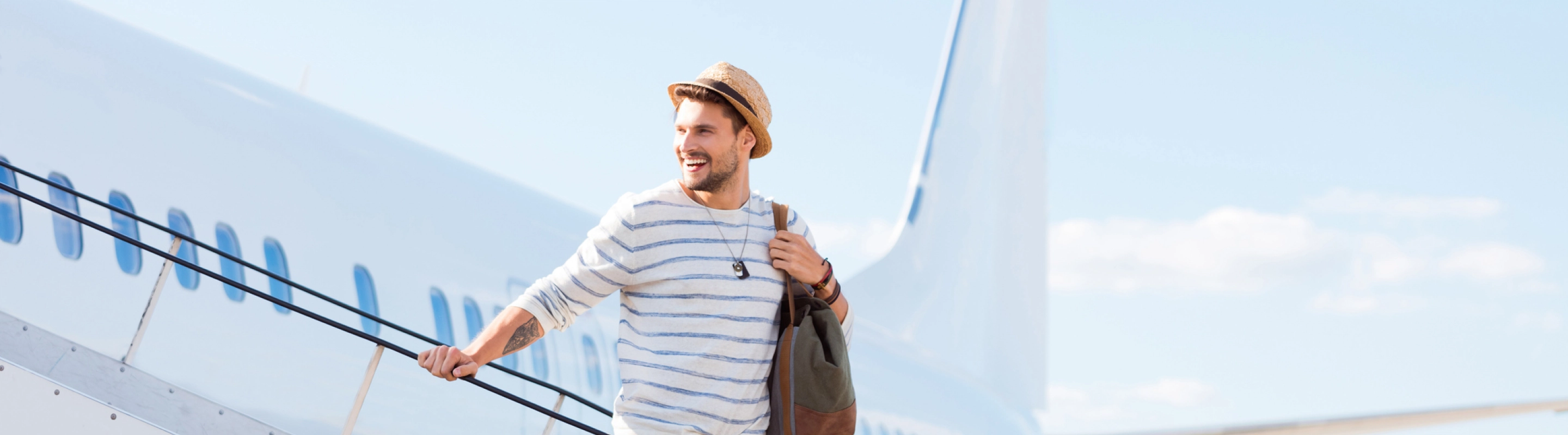 a young man wearing a hat and backpack walks down airplane boarding stairs, insured with solo travel insurance 