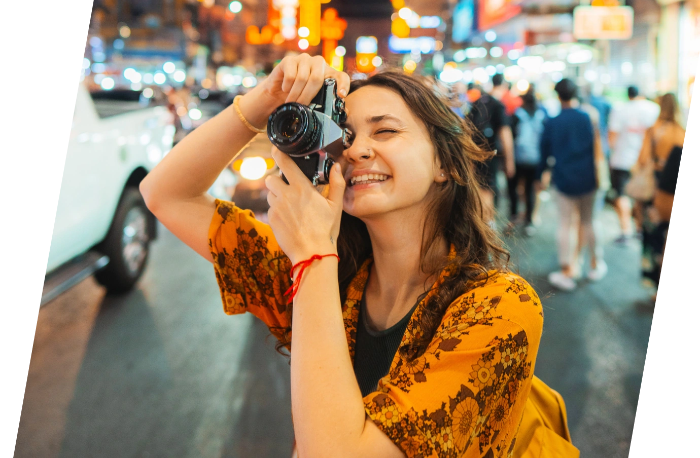 a young adult, brunette woman with travel insurance for students holds her camera up to take a photo on a busy city street