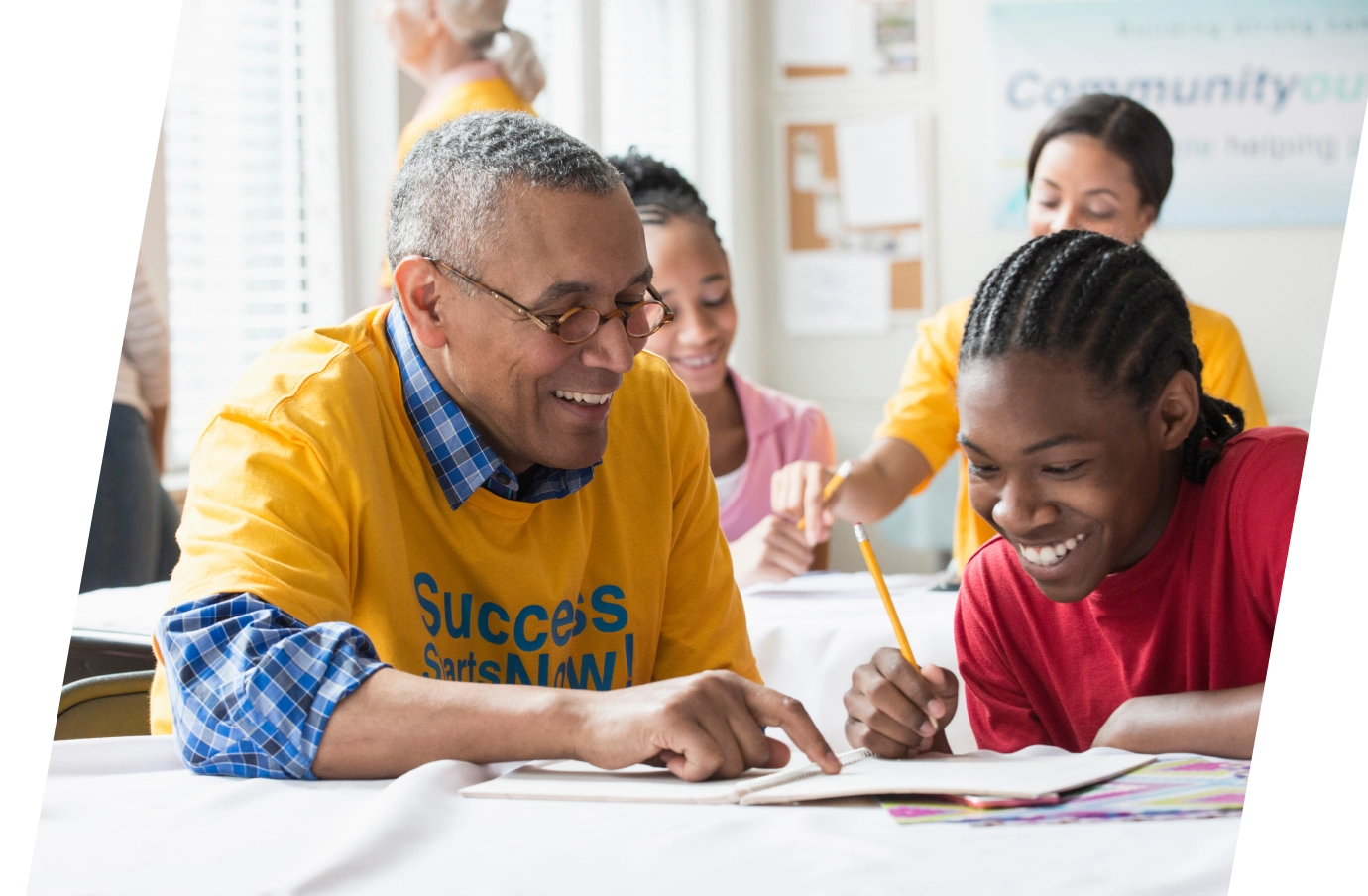 Older man with volunteer travel insurance tutoring a young man in a classroom