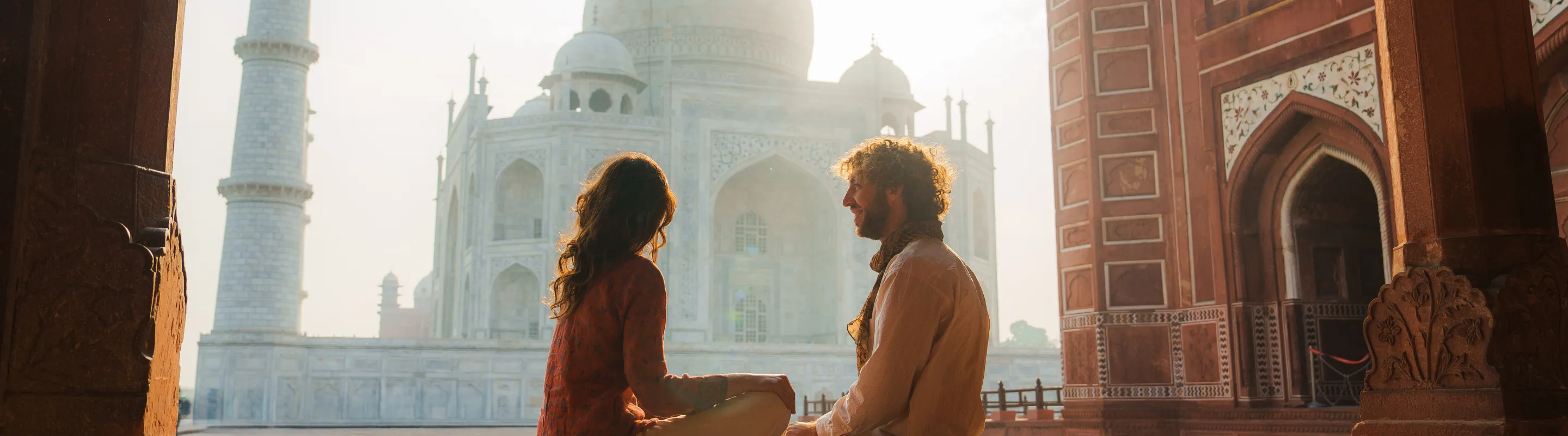 a couple with travel insurance for religious trips admires the Taj Mahal in India at sunrise 