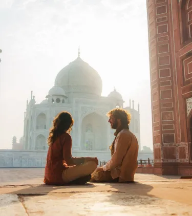 a couple with travel insurance for religious trips admires the Taj Mahal in India at sunrise 
