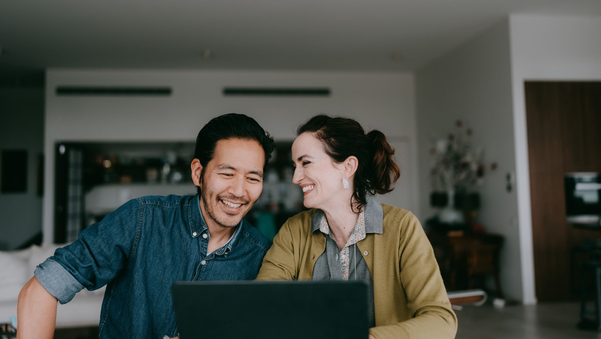 a young couple on laptop researches how to calculate their trip cost for travel insurance