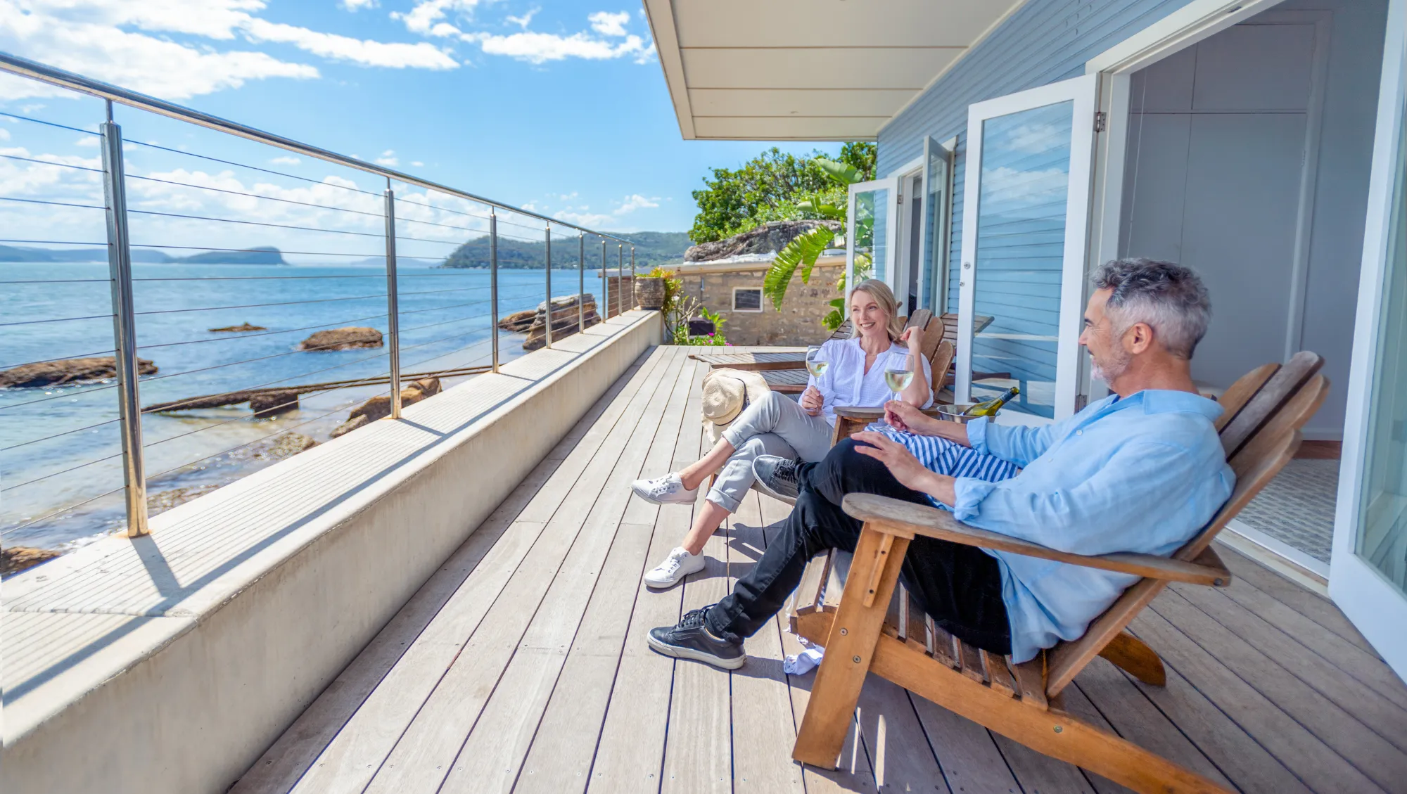 a couple relaxes on an oceanfront balcony on vacation after questioning "Is travel insurance worth it?"