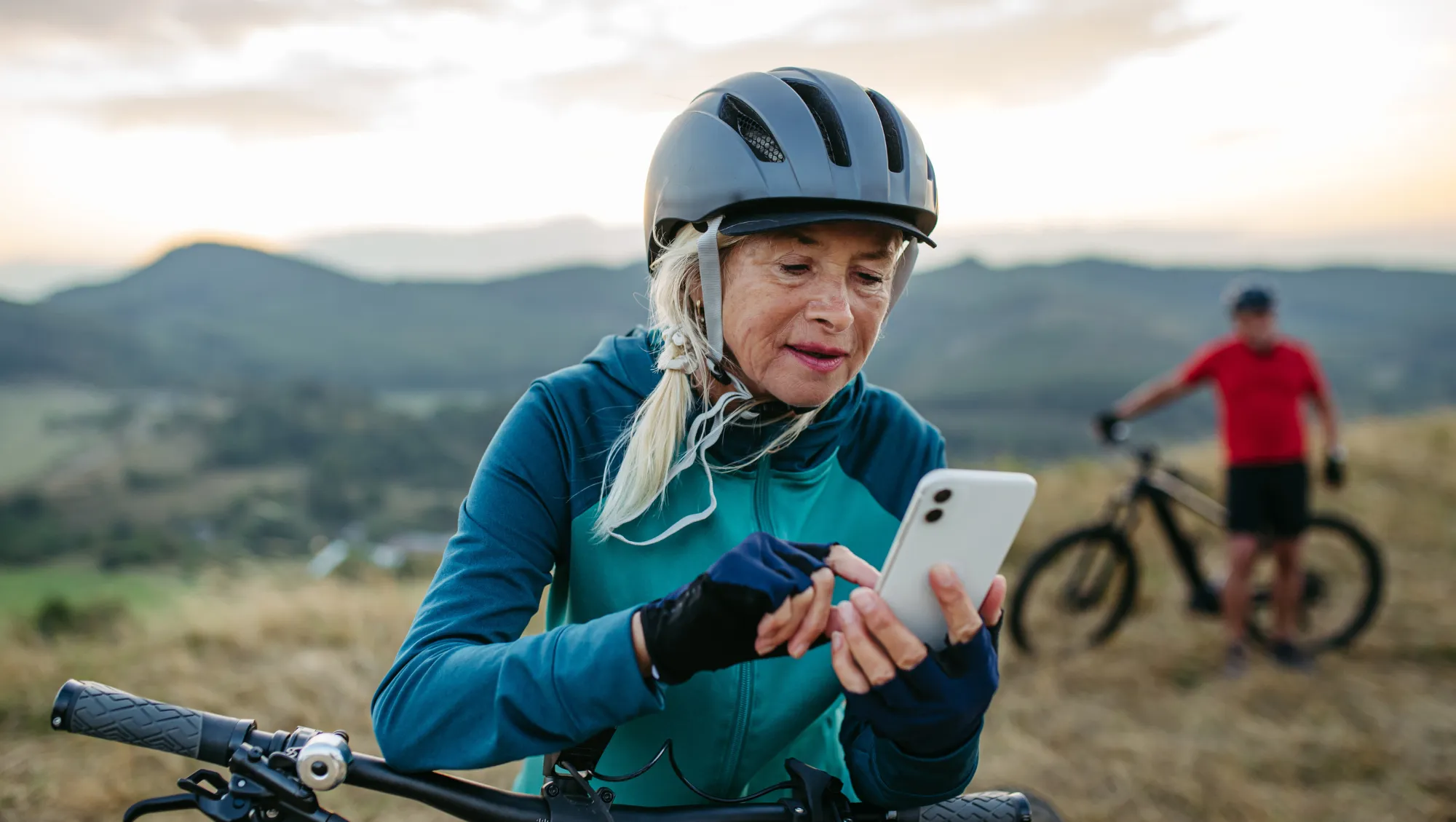 a female cyclist checks the travel app on her phone during a mountain bike ride with another cyclist 