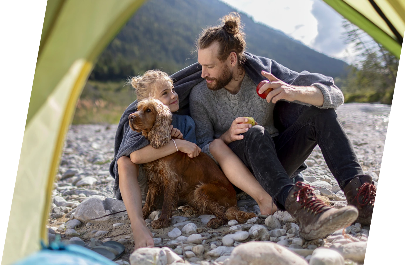 Father with pet travel insurance sitting with his son and dog on rocks and sharing a blanket
