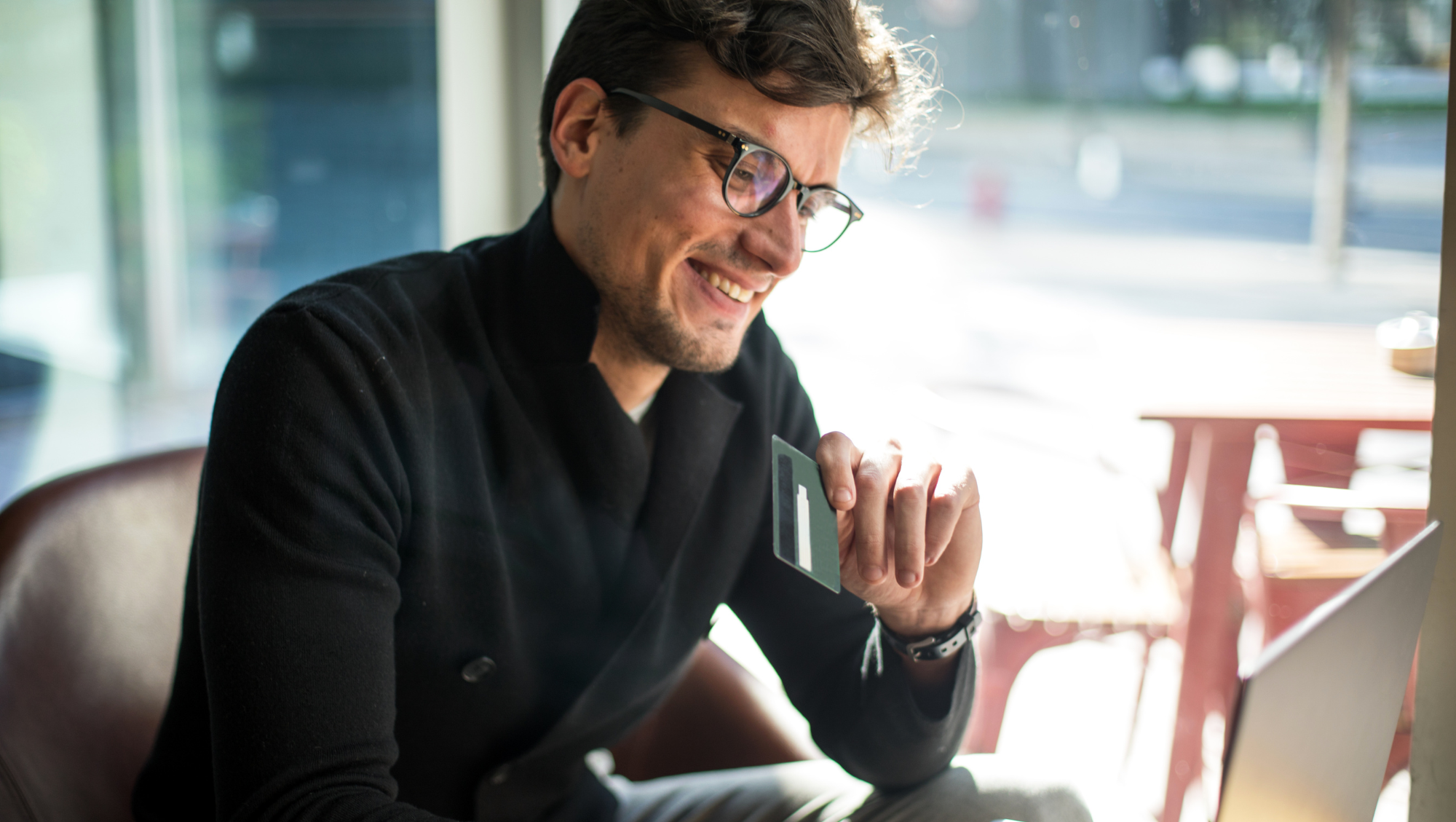 a man looks at a laptop and holds his credit card as he researches the pros and cons of credit card travel insurance 