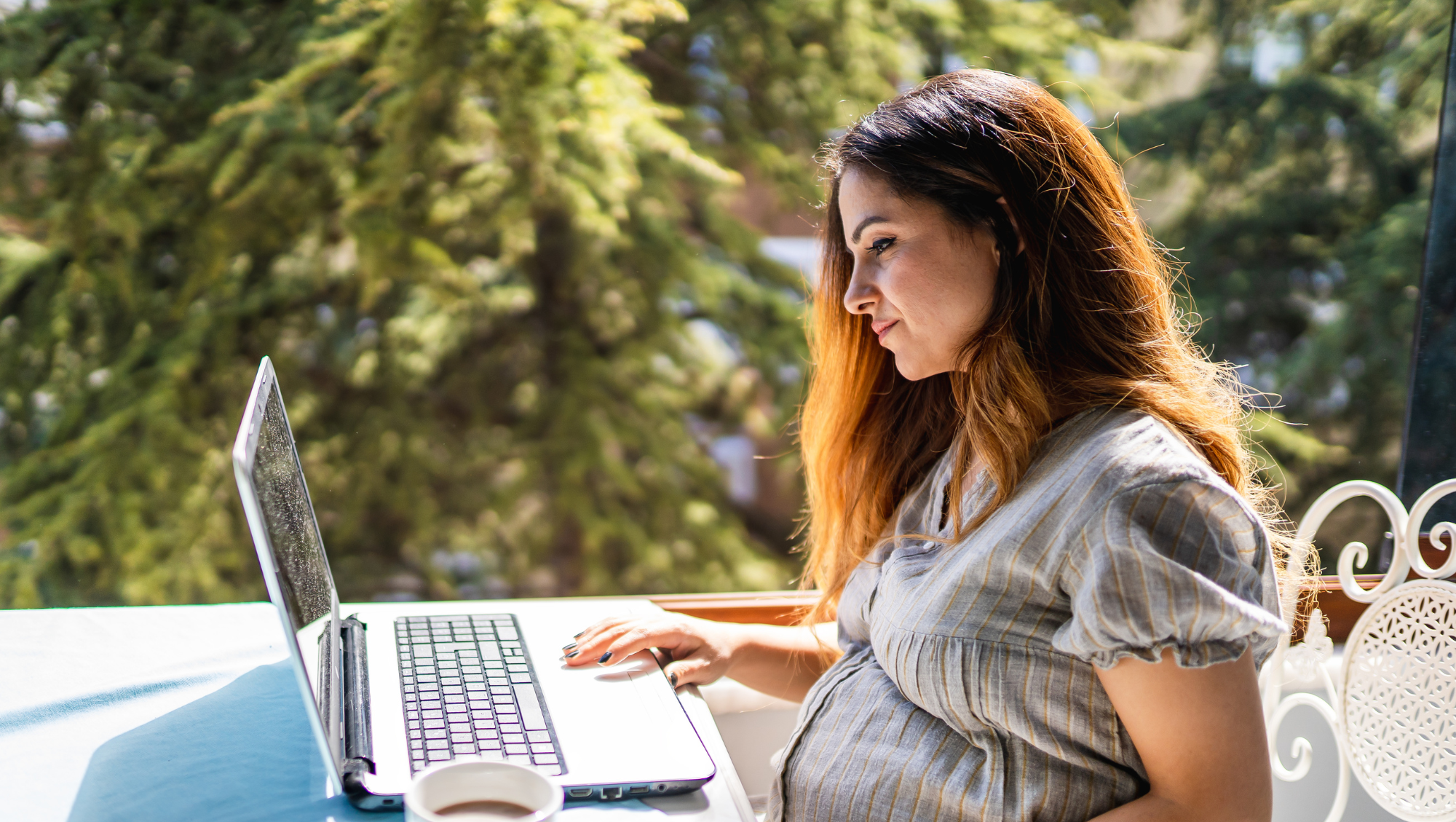 a pregnant woman sits on a laptop outdoors, looking up "How much is travel insurance?"